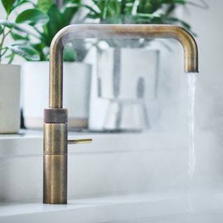 Brass boiling water tap on a white worktop, with steaming water