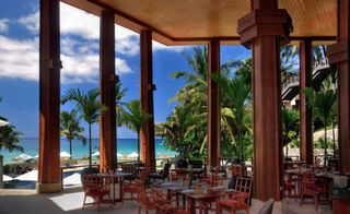 Surin hotel open air dining room with wooden pillars and ceiling, view of ocean and palm trees