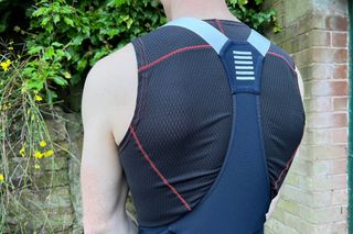 A close up of the back of the Rapha Pro Training tights showing a while male wearing them in a black sleeveless undervest in front of a stone wall and greenery