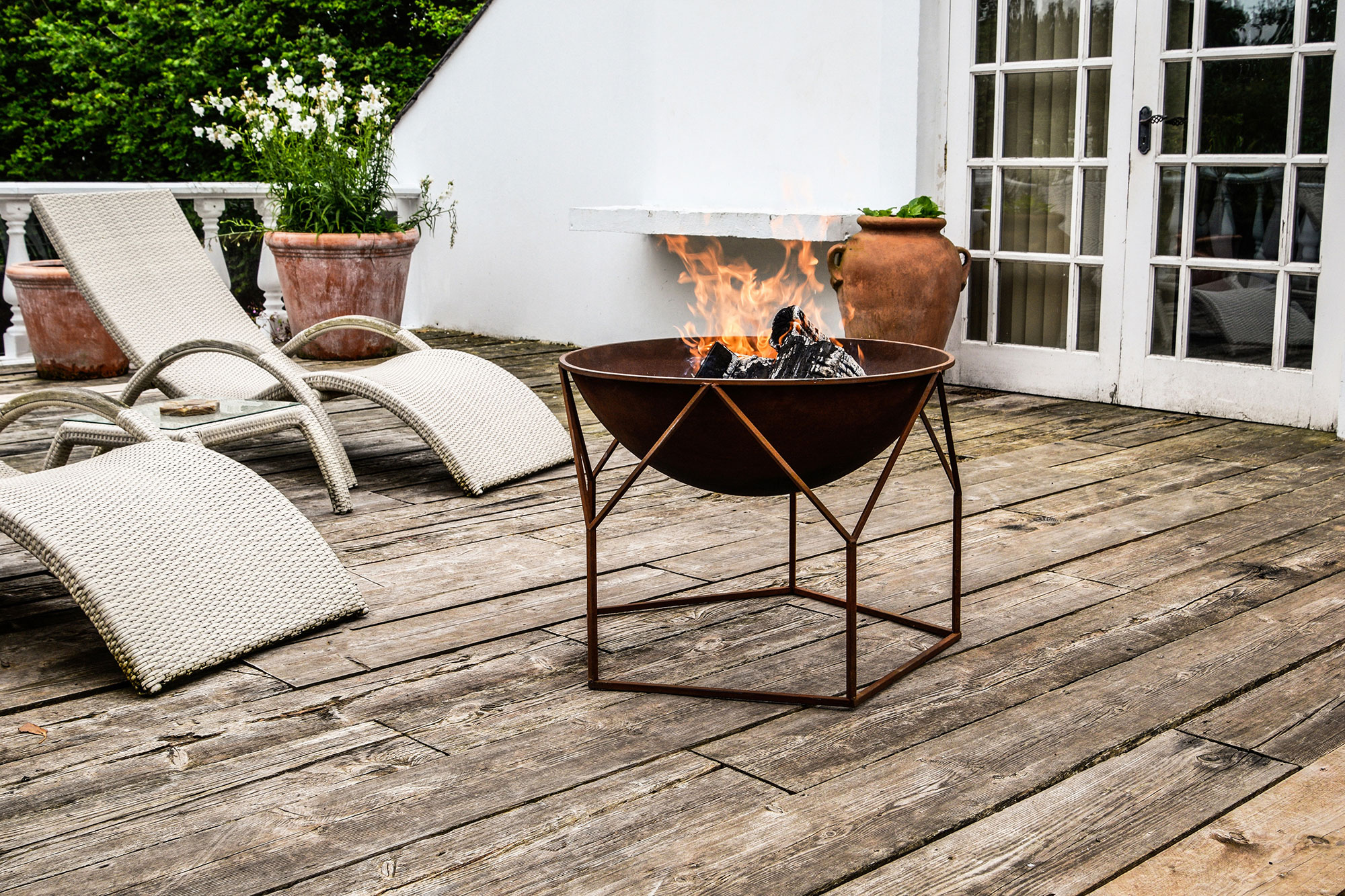 Rust fire pit on wooden deck with white loungers