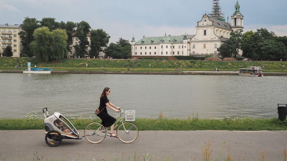 Woman riding bike next to river, with an impressive historic building on the other side