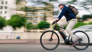 Man in casual business attire and bike helmet rides electric bike