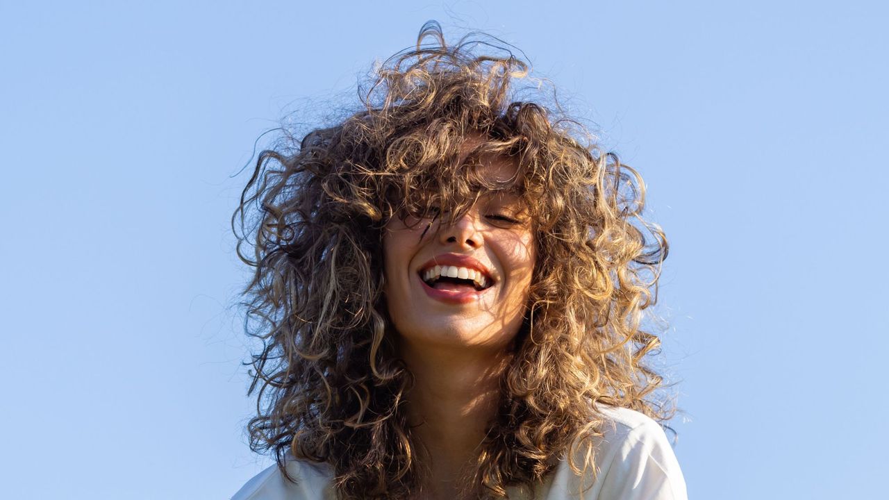 best shampoo for dandruff - Woman smiling with wavy hair and blue skies behind her gettyimages -1667792390