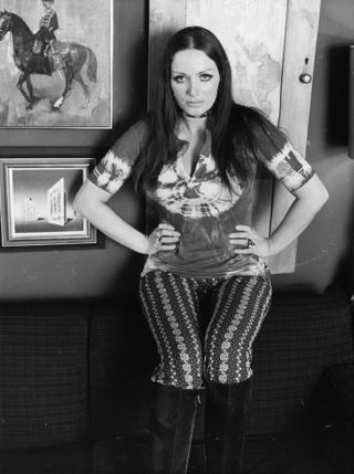 March 1971: English novelist Jackie Collins (1937 - 2015) wearing a tie-dye t-shirt and patterned leggings.