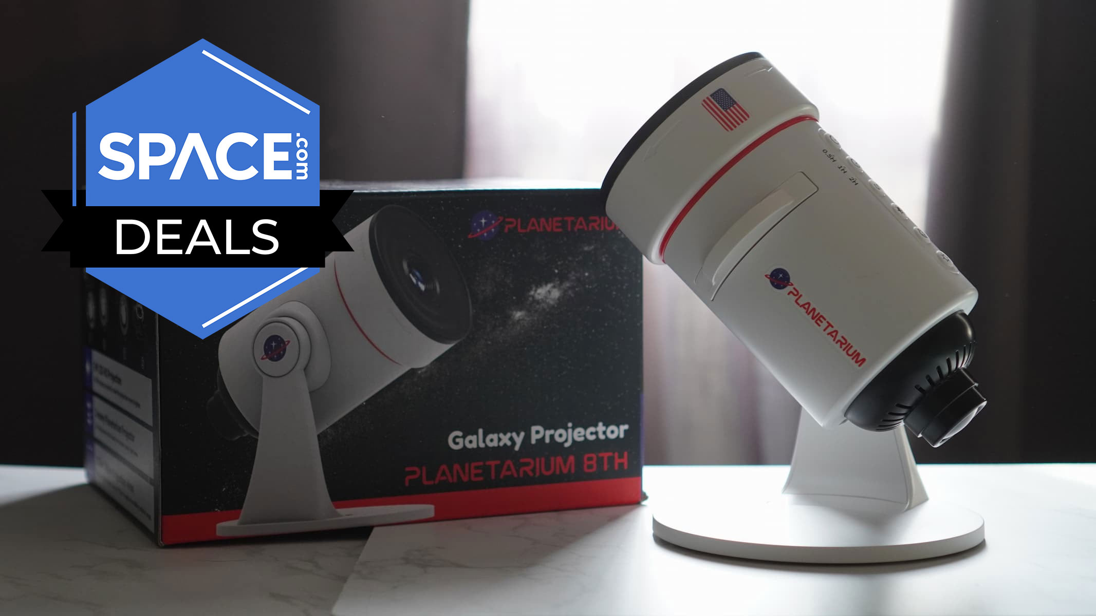 A white microscope-looking projector is attached to a white stand and is on a white surface in front of a window in the background. It's next to a black product box with the space.com logo in the top left.