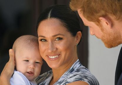 Meghan Markle holds baby Archie while smiling next to husband Prince Harry.