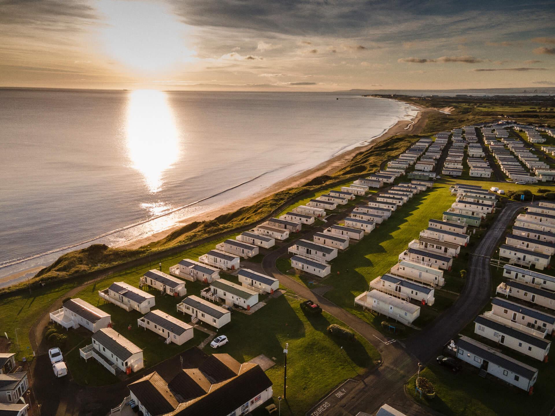  a row of caravans opposite a beach during sunset 