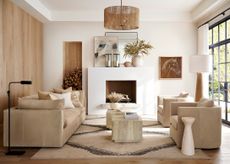 a contemporary living area with a neutral color palette with a beige sofa facing two beige armchairs with a rectangular coffee table in the middle with a modern mantelpiece at the back of the room with a mirror, artwork and foliage on display