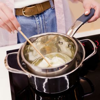 Woman melts wax in a pot for candles over an induction hob