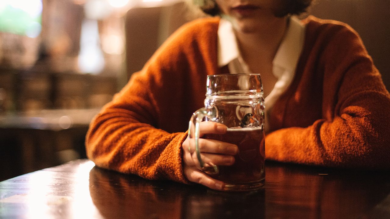 Young woman holding beer glass while sitting in the pub