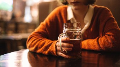 Young woman holding beer glass while sitting in the pub