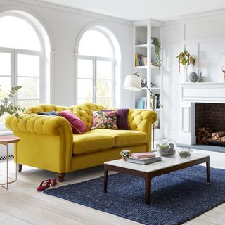 white living area with fire place yellow sofa and blue carpet