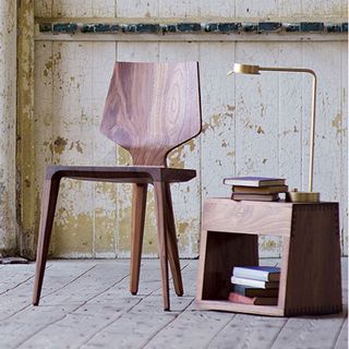 Dark wood De La Espada dining chair next to a matching side table in a rustic room.