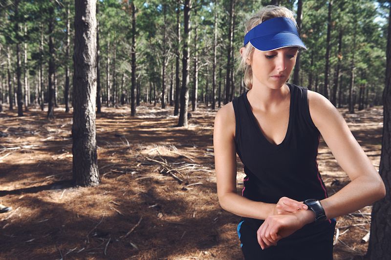 A woman checks her fitness watch while walking in the woods.