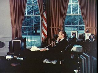President Gerald R. Ford watches ASTP crewmen Thomas P. Stafford, Donald K. Slayton and Valeriy N. Kubasov on television as he talks to them via radio-telephone while they orbited the Earth on July 18, 1975.