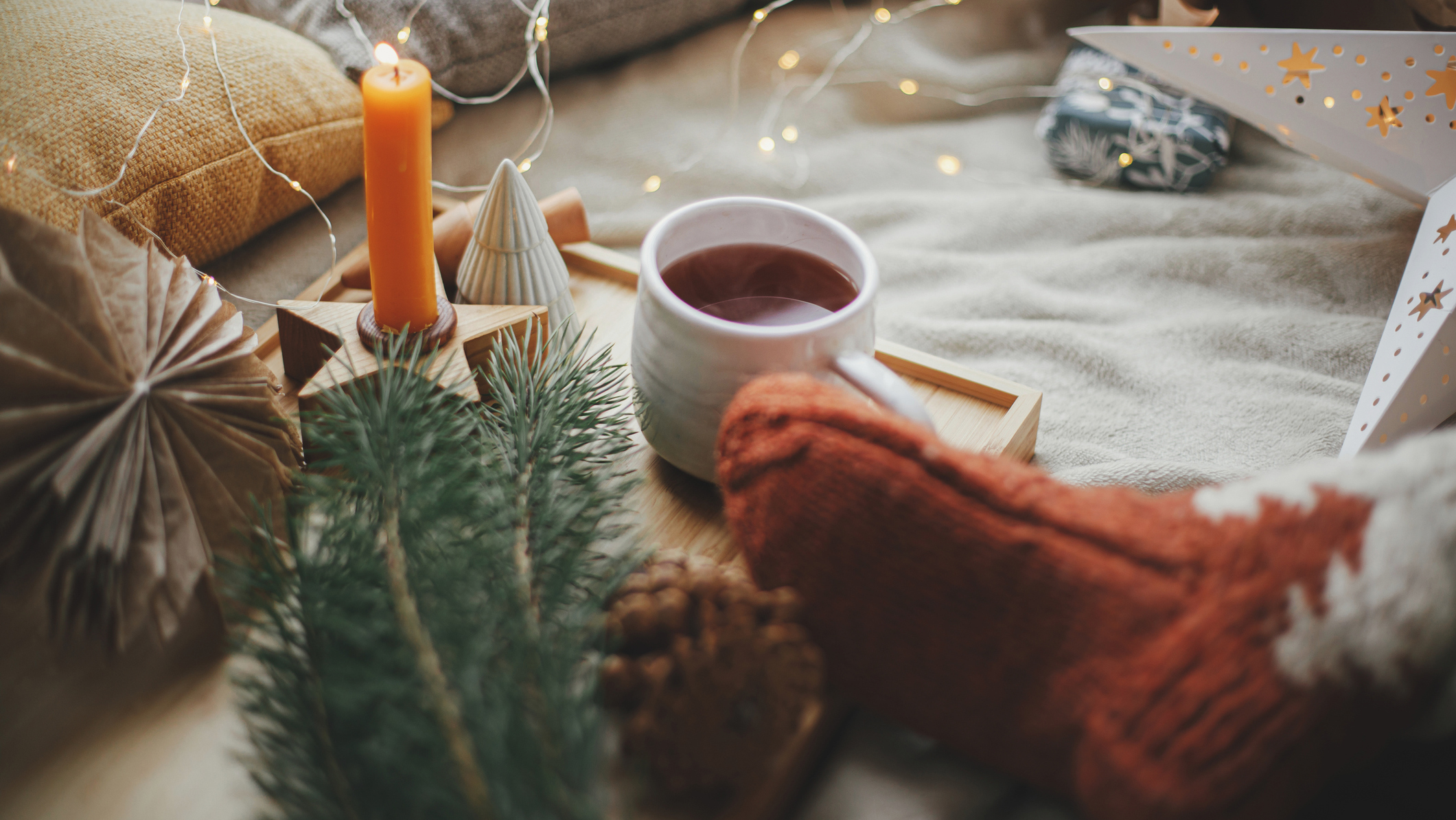 Ideas for how to decorate for Christmas showing a pine cone, pine needles, a candle, a porcelain Christmas tree, woollen socks and a mug of hot chocolate