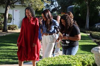 Meghan Markle walks with teens while wearing a blue shirt and white pants