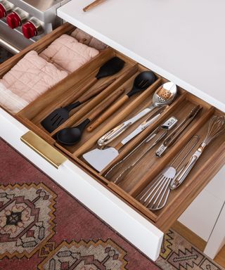 A wooden kitchen drawer with silver and black cutlery and utensils in it