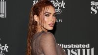 Megan Fox attends the Sports Illustrated Swimsuit issue party in 2023. She is standing on the red carpet and staring at the camera in a long sleeve dress. Her hair is wet.