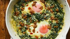 eggs in creamed spinach with spiced butter seeds in a white skillet