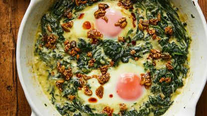 eggs in creamed spinach with spiced butter seeds in a white skillet