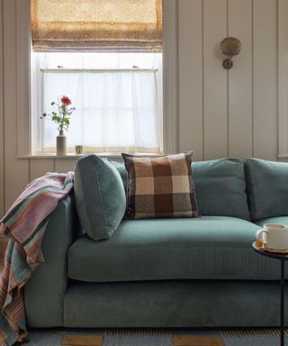 vintage neutral panelled living room with a blue velvet couch and a layered window with patterned blind and a cafe curtain