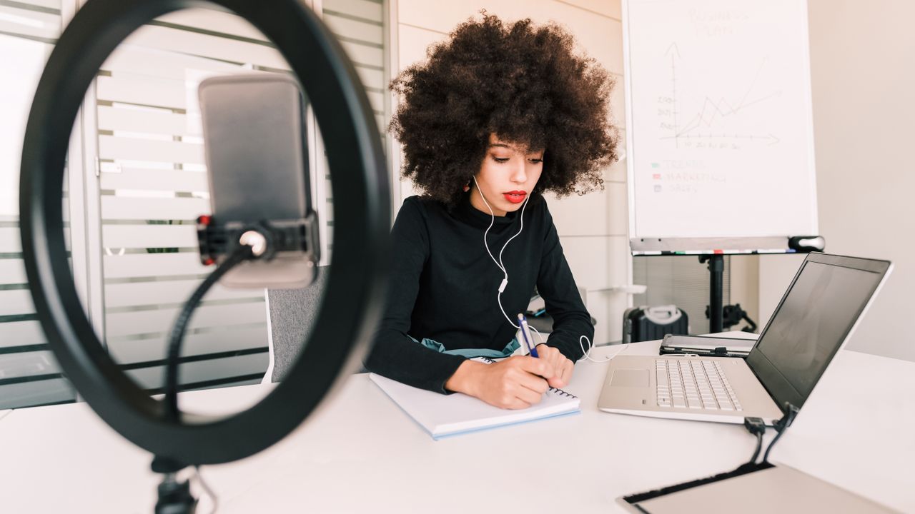 Woman working on a laptop wiith a camera and ring light pointed at her