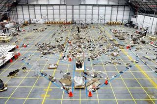 An overview of the Columbia debris reconstruction hangar in 2003 shows the orbiter outline on the floor with some of the 78,760 pieces identified to that date. More than 84,000 pieces of shuttle debris were recovered, some of which is included in a traveling NASA display to stress safety.