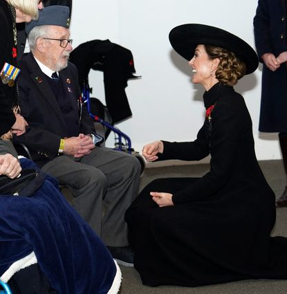 Kate Middleton kneeling in a black coat and hat talking to veterans in wheelchairs