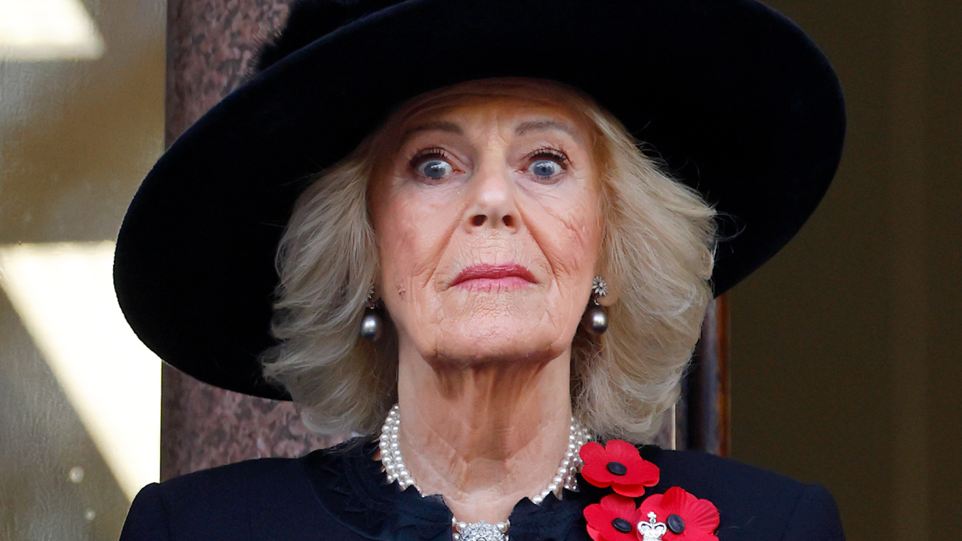 Queen Camilla wearing a big black hat looking surprised