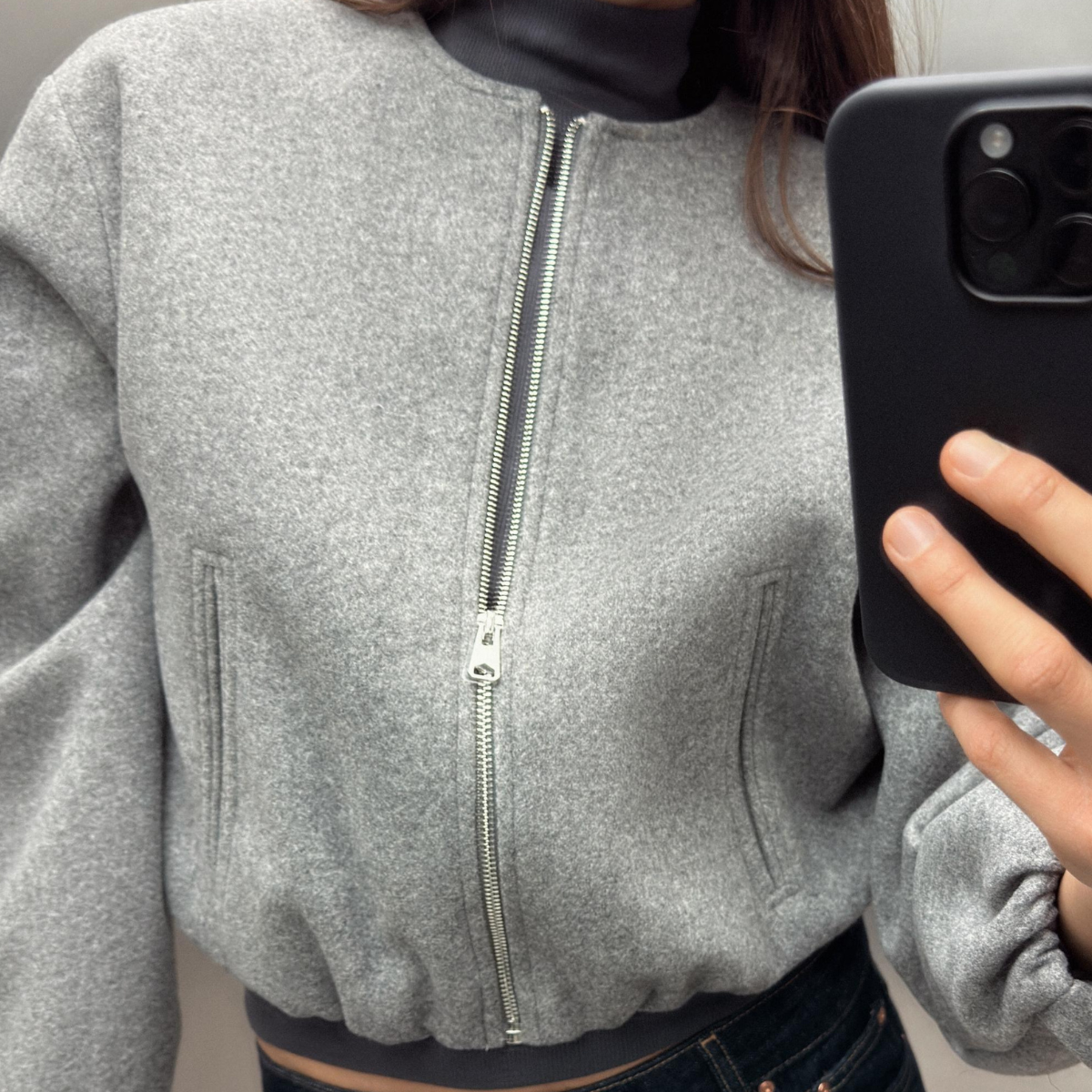 Woman taking a mirror selfie wearing a gray Zara bomber jacket with jeans.