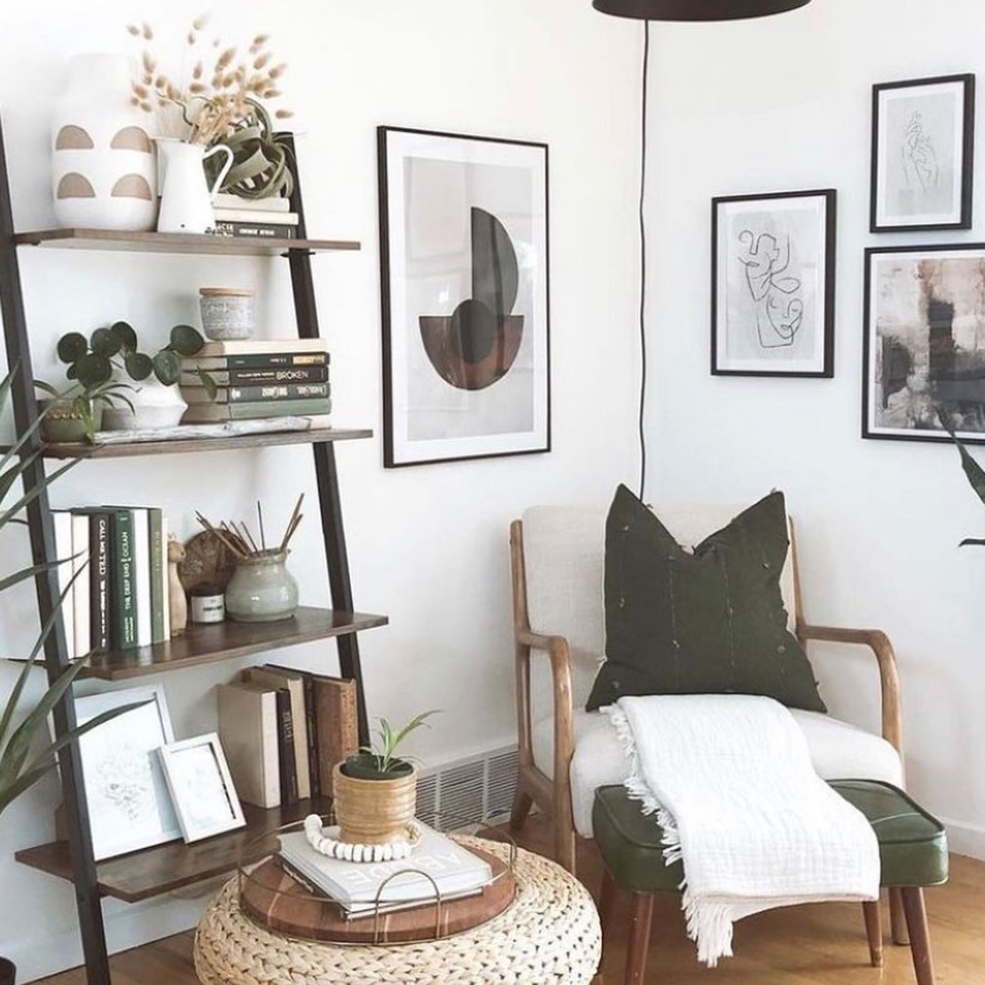 Sudut baca yang nyaman dengan kursi yang nyaman, sandaran anyaman dan rak terbuka dengan buku, dalam palet netral dan mono yang tenang.