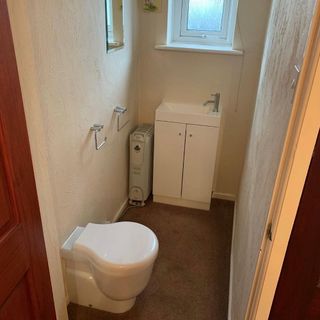 a small cloackroom with brown carpet and white toilet and vanity unit, with a radiator tucked next to the sink