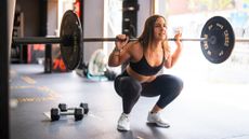 A woman holds a barbell on her shoulders and executes a squat in a gym.