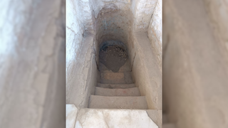 Photograph looking down a short set of marble stairs into a narrow, empty pool with an apsidal end