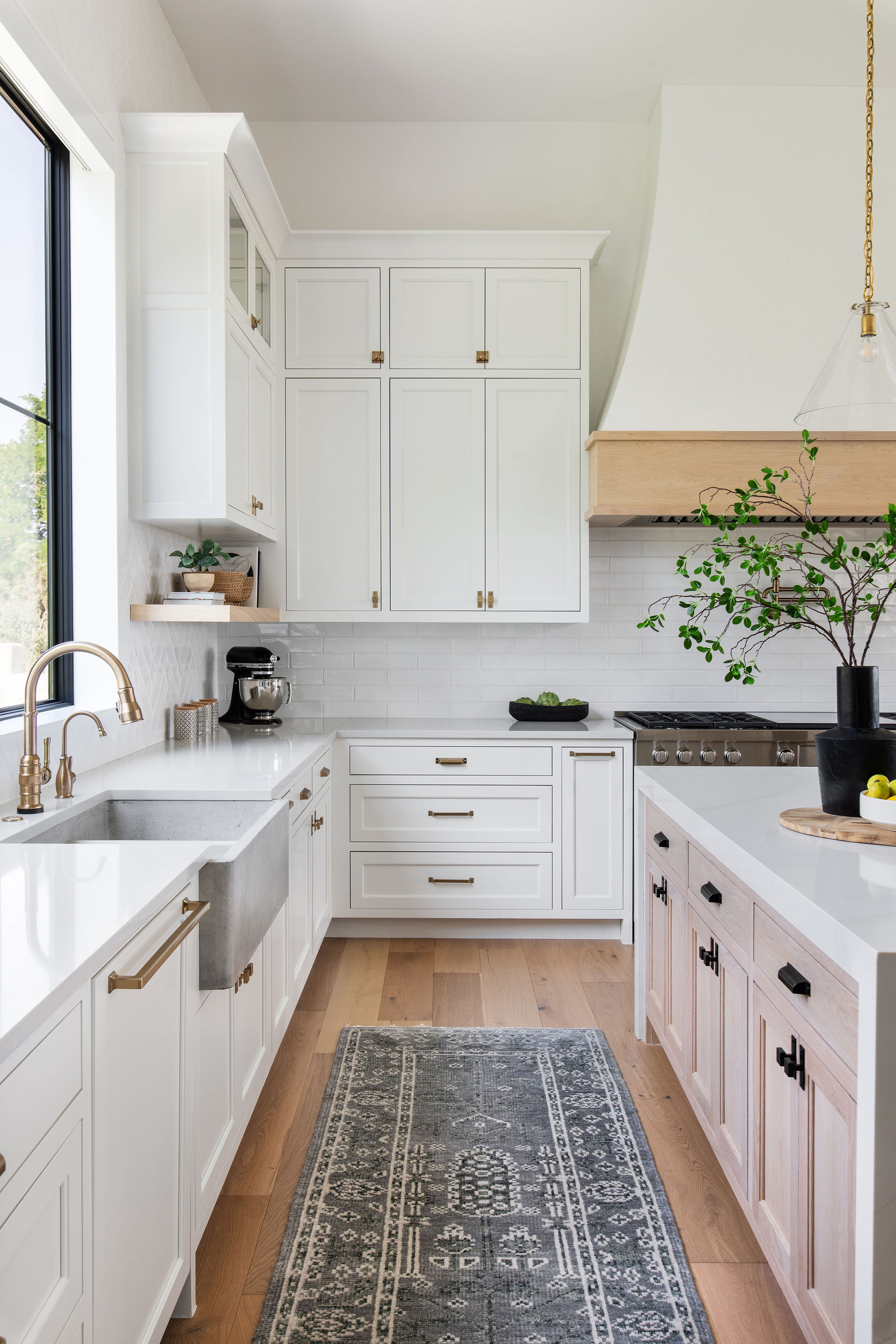 A white kitchen with white quartz countertops, a blue patterned runner, and wooden flooring