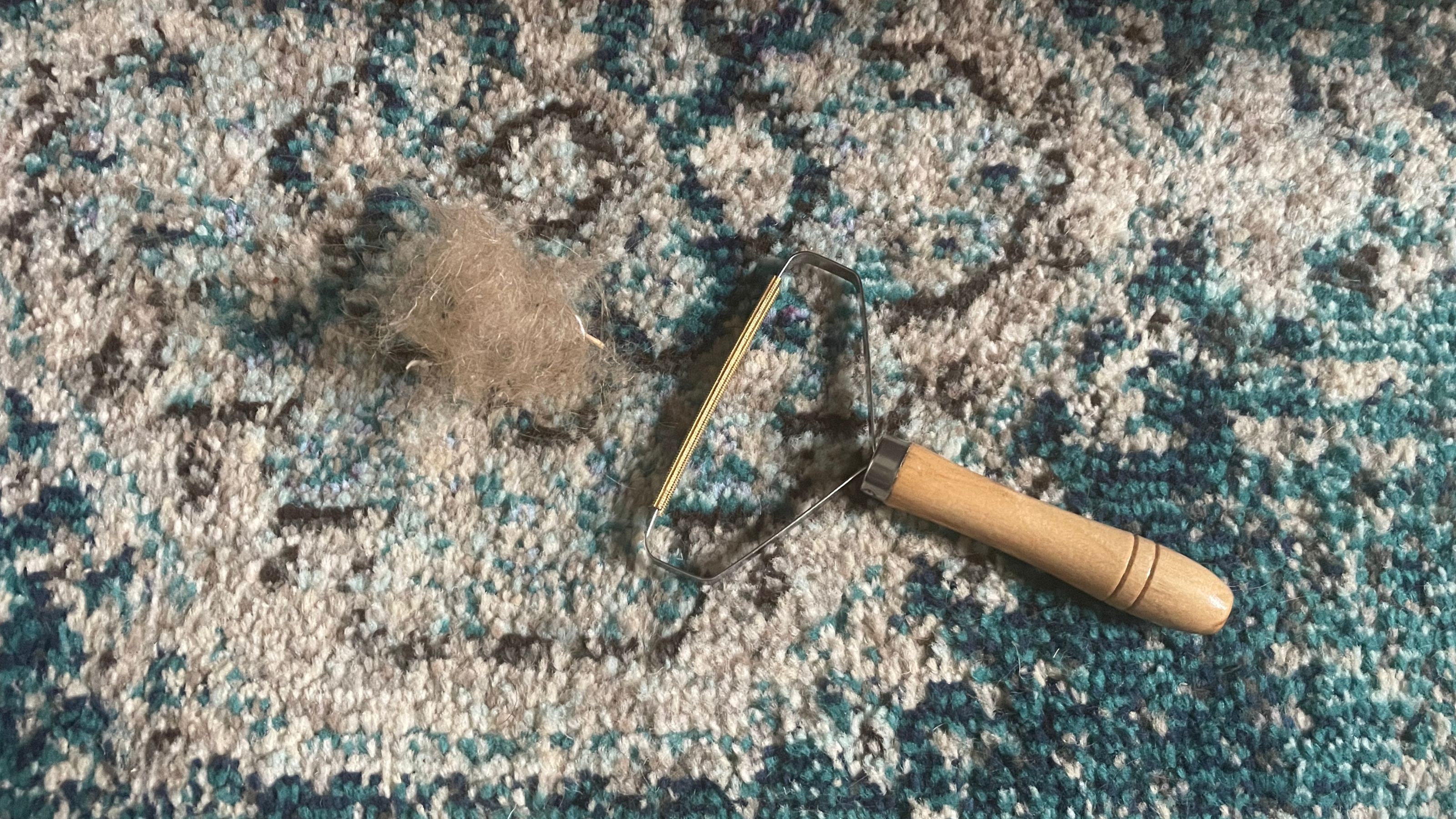 carpet scraper on a blue patterned rug, with a hairball next to it