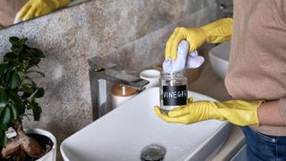 Someone wearing gloves cleaning a bathroom with vinegar