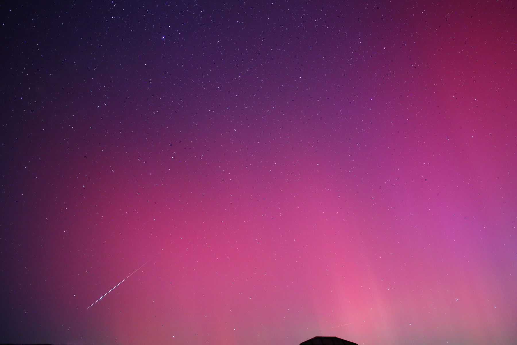 Perseid meteor shower against a pink sky colored by aurora borealis