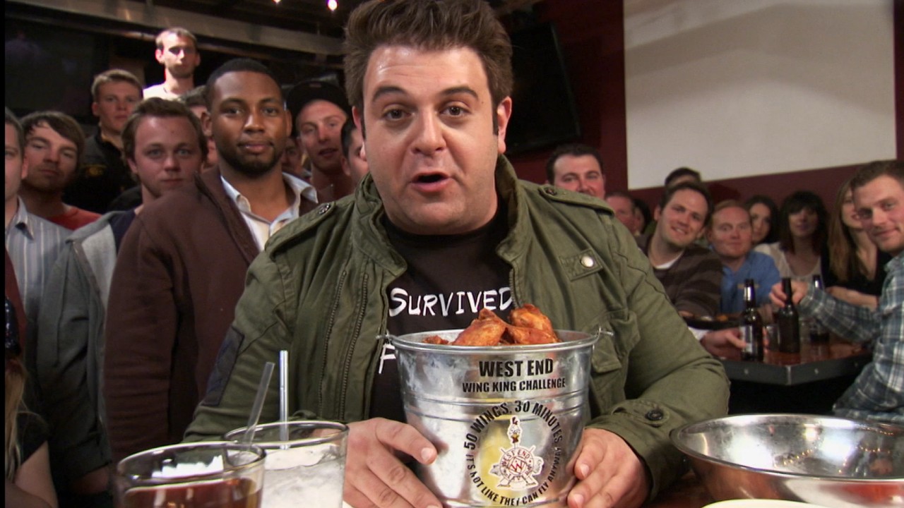 Adam Richman sitting in front of a bucket full of wings