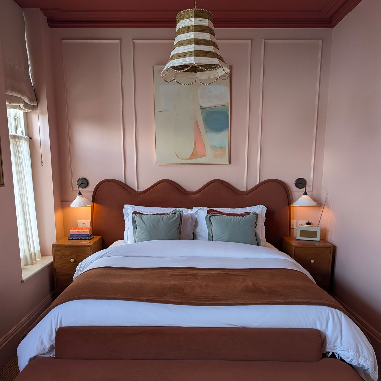 Bedroom with pink panelled walls, red ceiling, striped pendant light shade, two wall lights on either side of bed with wavy headboard