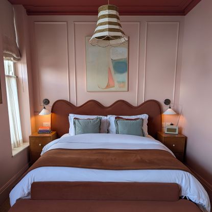 Bedroom with pink panelled walls, red ceiling, striped pendant light shade, two wall lights on either side of bed with wavy headboard
