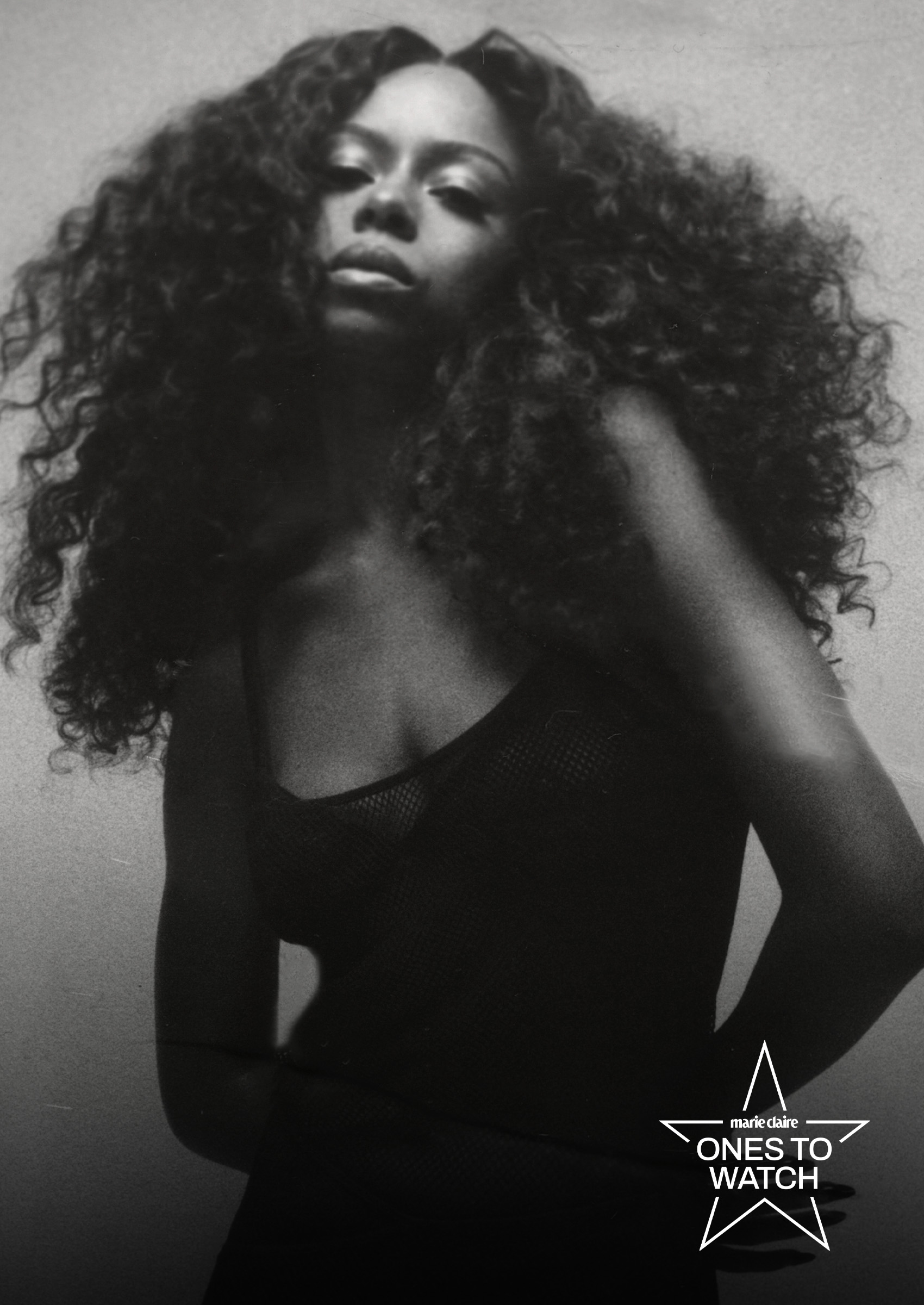 ravyn lenae poses in a black and white photo with her hair draped over her shoulders and with her hands behind her back