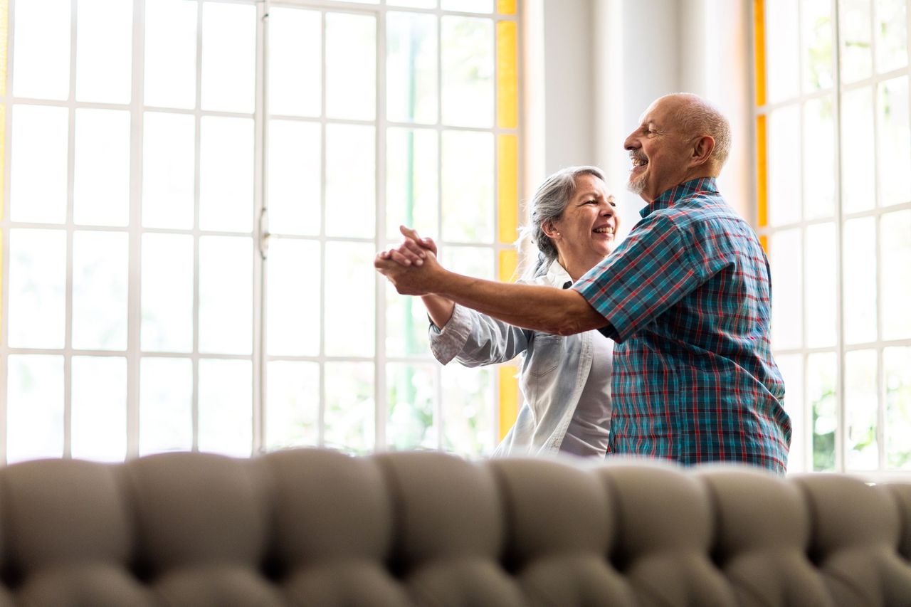 A happy couple dance together in their living room. 