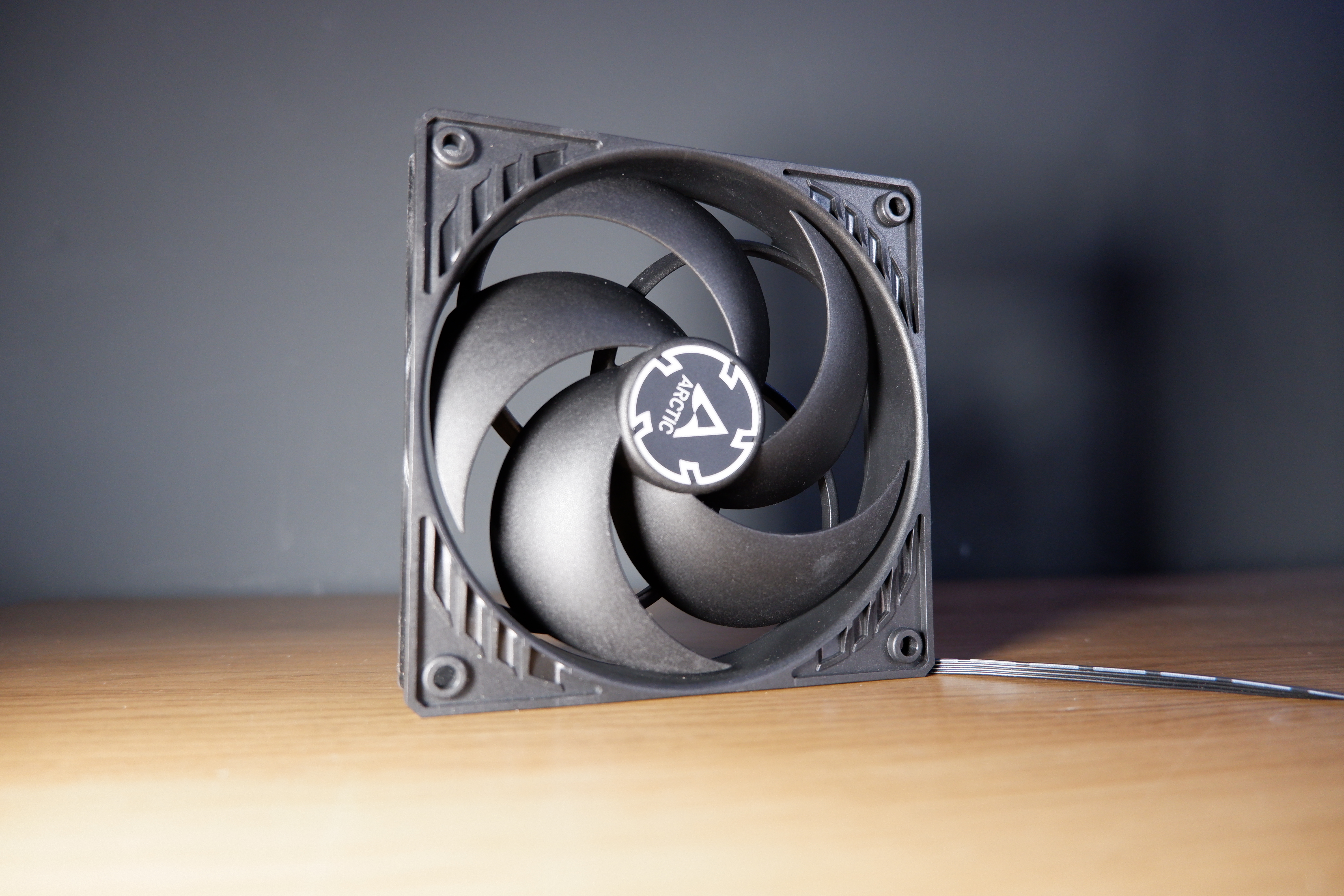 The Arctic P12 PWM PST in black sits on top of a desk.