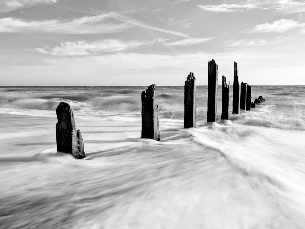 A damaged groyne on a UK beach, the high tide is smashing into it, with the moving water blurred using a long exposure photography technique