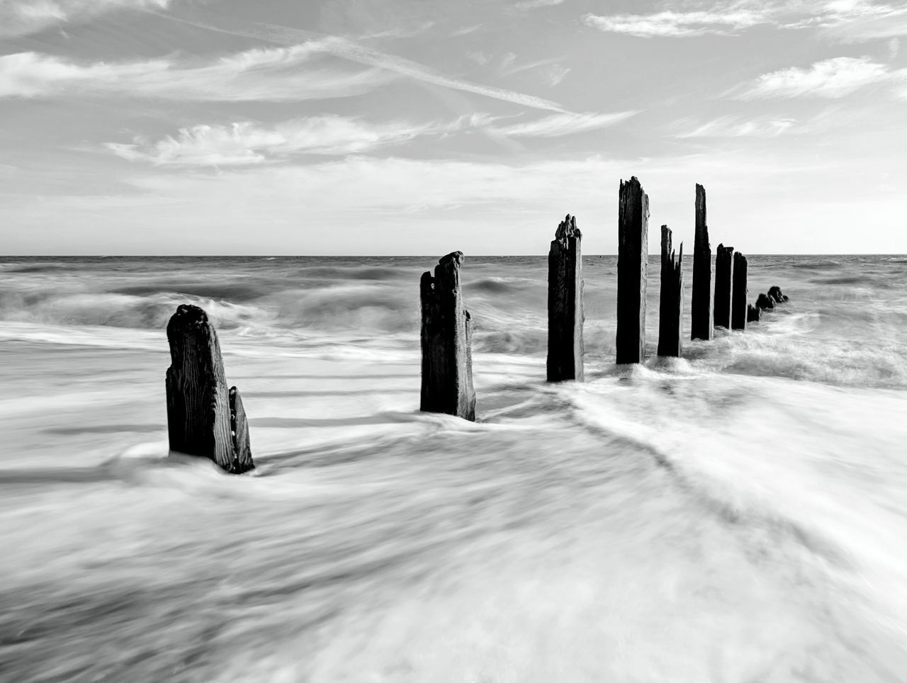 A damaged groyne on a UK beach, the high tide is smashing into it, with the moving water blurred using a long exposure photography technique
