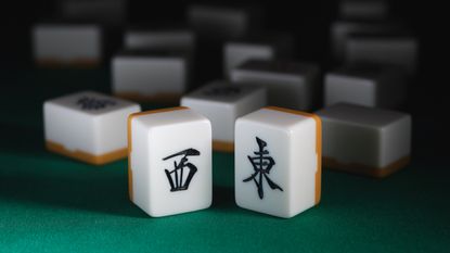 Two upright mahjong tiles on green velvet with other tiles in the background.