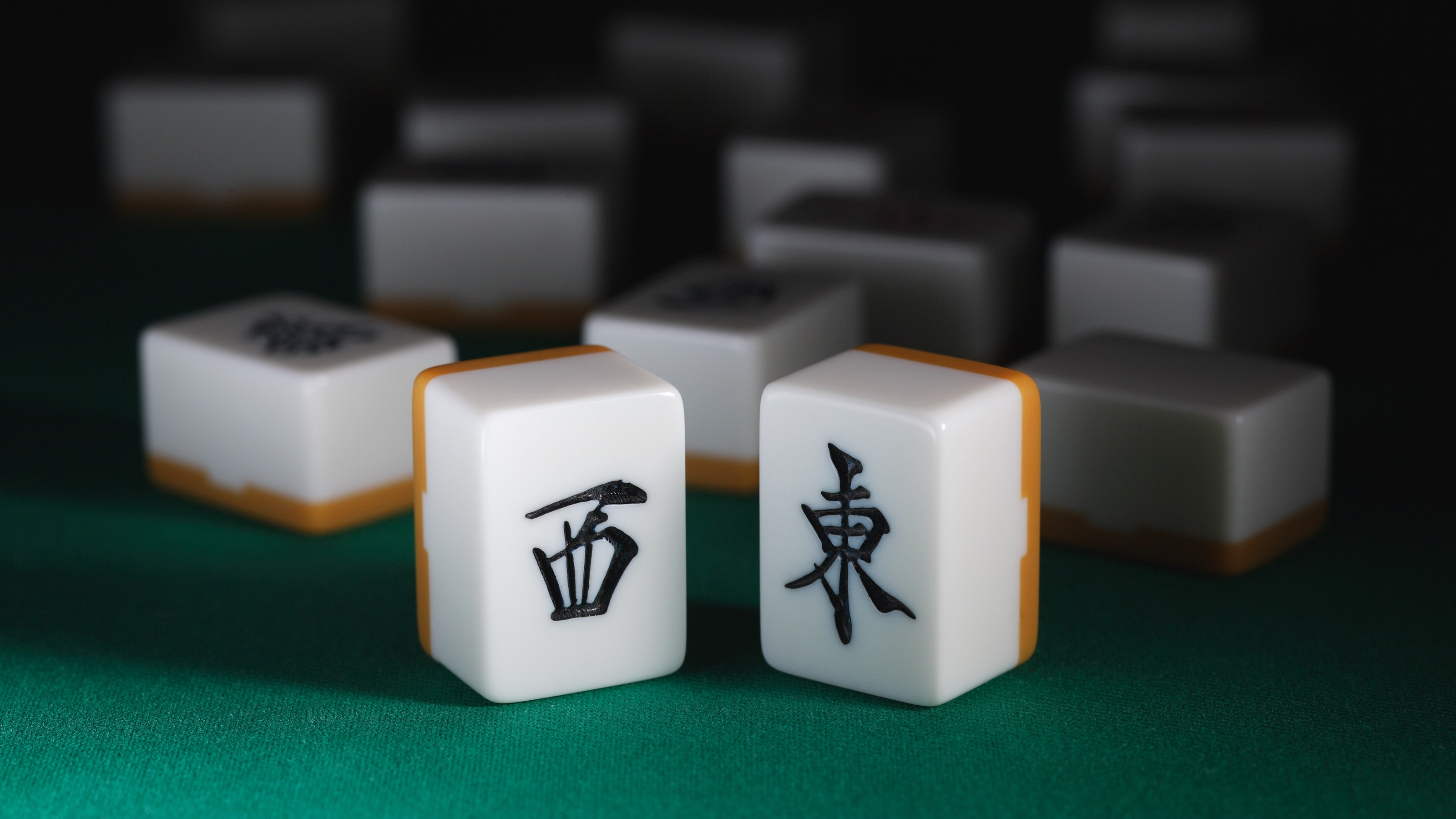 Two upright mahjong tiles on green velvet with other tiles in the background.
