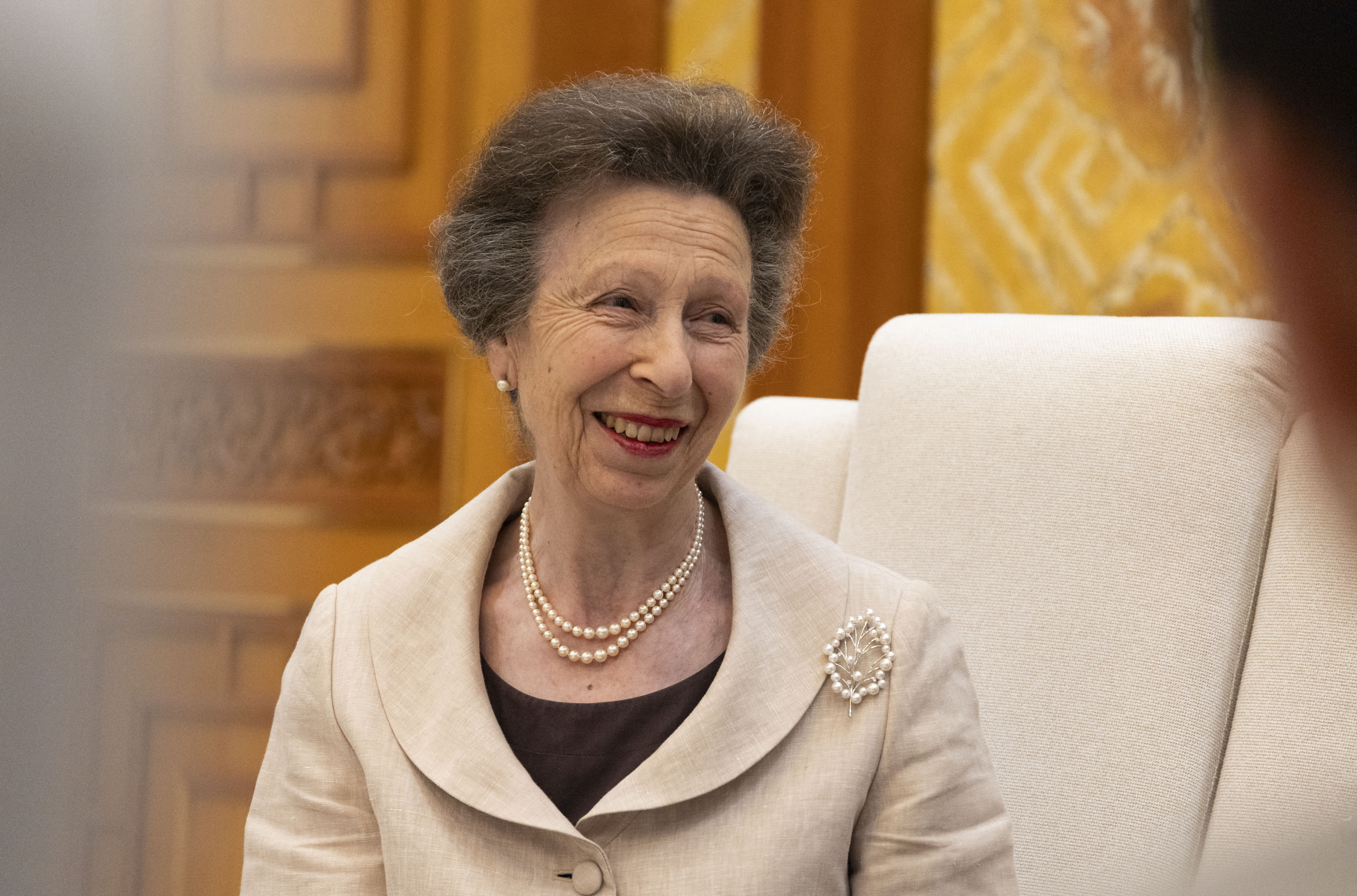 Princess Anne smiling in a pearl necklace and tan jacket